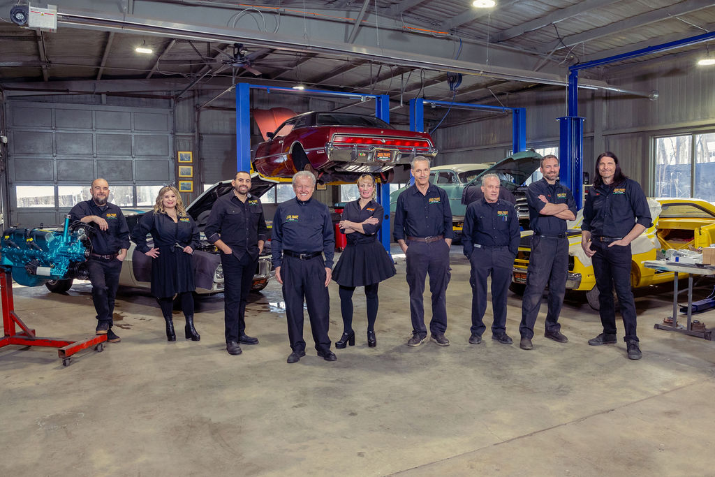 The Jack Frost team in a line in front of cars in various states of restoration in the shop